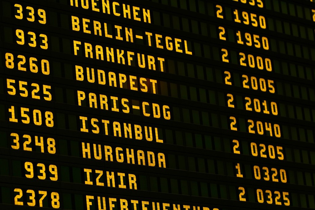 An electronic travel departures board at an airport on a black background with yellow writing.